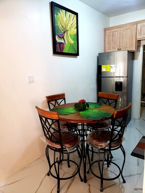 A dining area with a round table, four chairs, and a refrigerator.