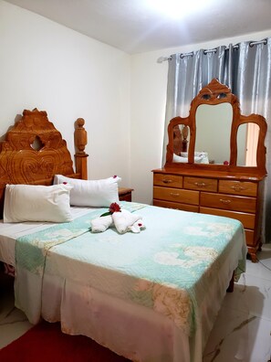 A neatly made bed with a floral bedspread, a wooden headboard, and a wooden dresser with a mirror.