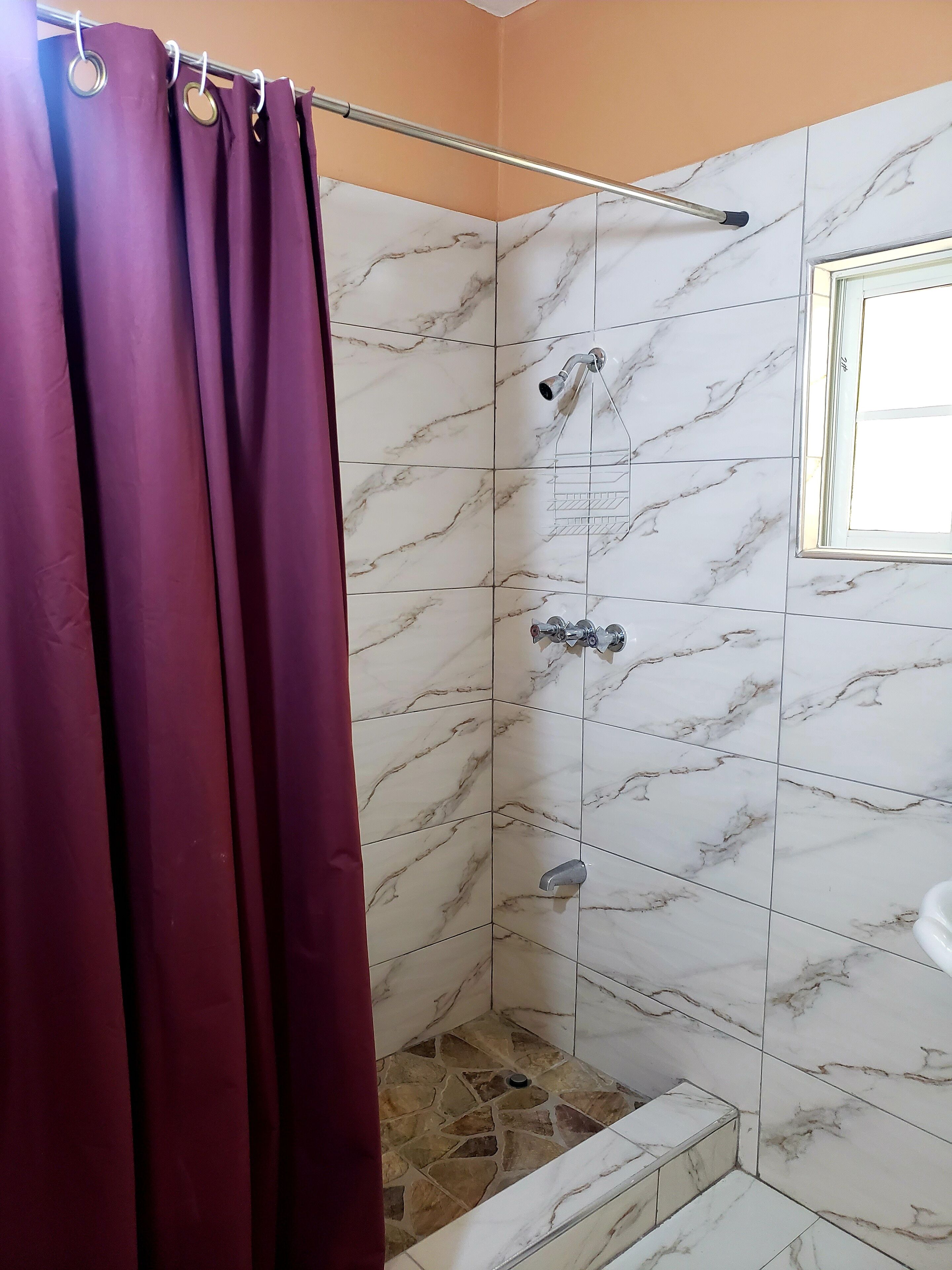 A shower area with marble tiles, a showerhead, and a window.