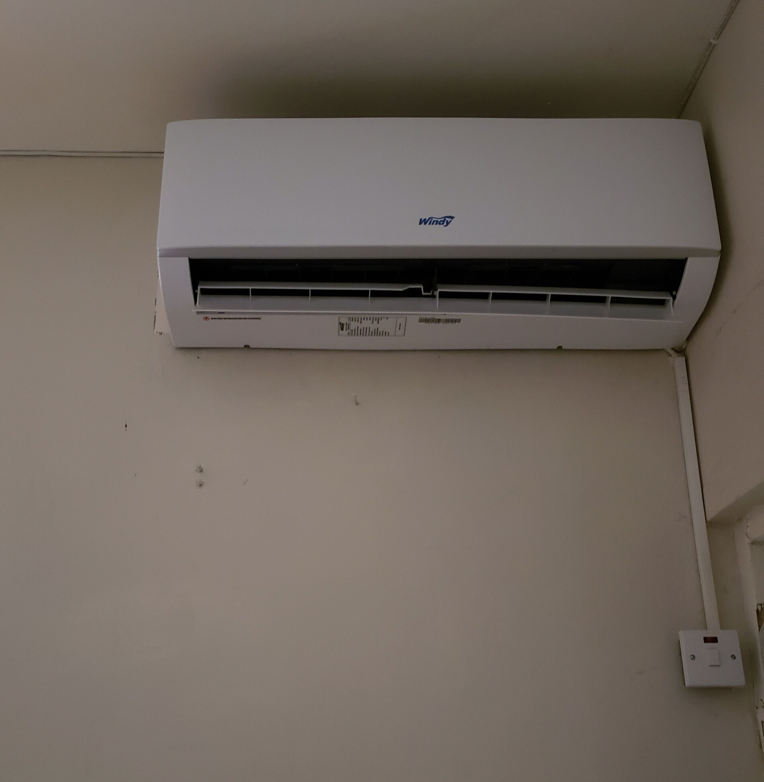 Een wit hangende airconditioner met een zichtbaar logo en een stopcontact.