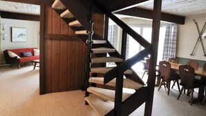 Una escalera de caracol con peldaños alfombrados y barandillas de madera en una habitación con una mesa de comedor y sillas, un sofá rojo y un cuadro en la pared.