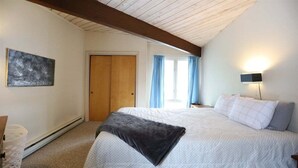 Un dormitorio con cama, mesita de noche, lámpara de pared, puerta y ventana con cortinas.