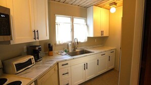 Una cocina con armarios blancos, microondas integrado, tostadora, cafetera y un lavamanos.