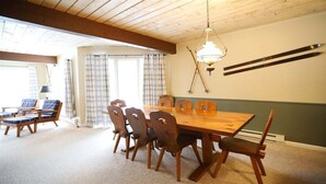 Un comedor con mesa y sillas de madera, una araña y vistas al exterior.