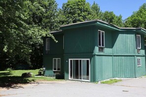 Um edifício verde com telhado plano, janelas amplas e porta de correr de vidro.