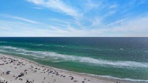 Een strand met mensen en parasols, een heldere lucht en de oceaan.