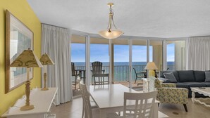 Een kamer met een eettafel, stoelen, een bank en een balkon met uitzicht op zee.