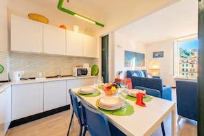 A modern kitchen with white cabinets, a microwave, and a dining area with a table set for two. - Portofino Apartment Sea View Dream (Portofino)