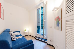 Een kamer met een blauwe bank, een tafeltje met een lamp en een deur naar een balkon.