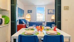 Un coin repas avec une table dressée pour quatre personnes, une vue sur la rue et une fenêtre avec des volets.