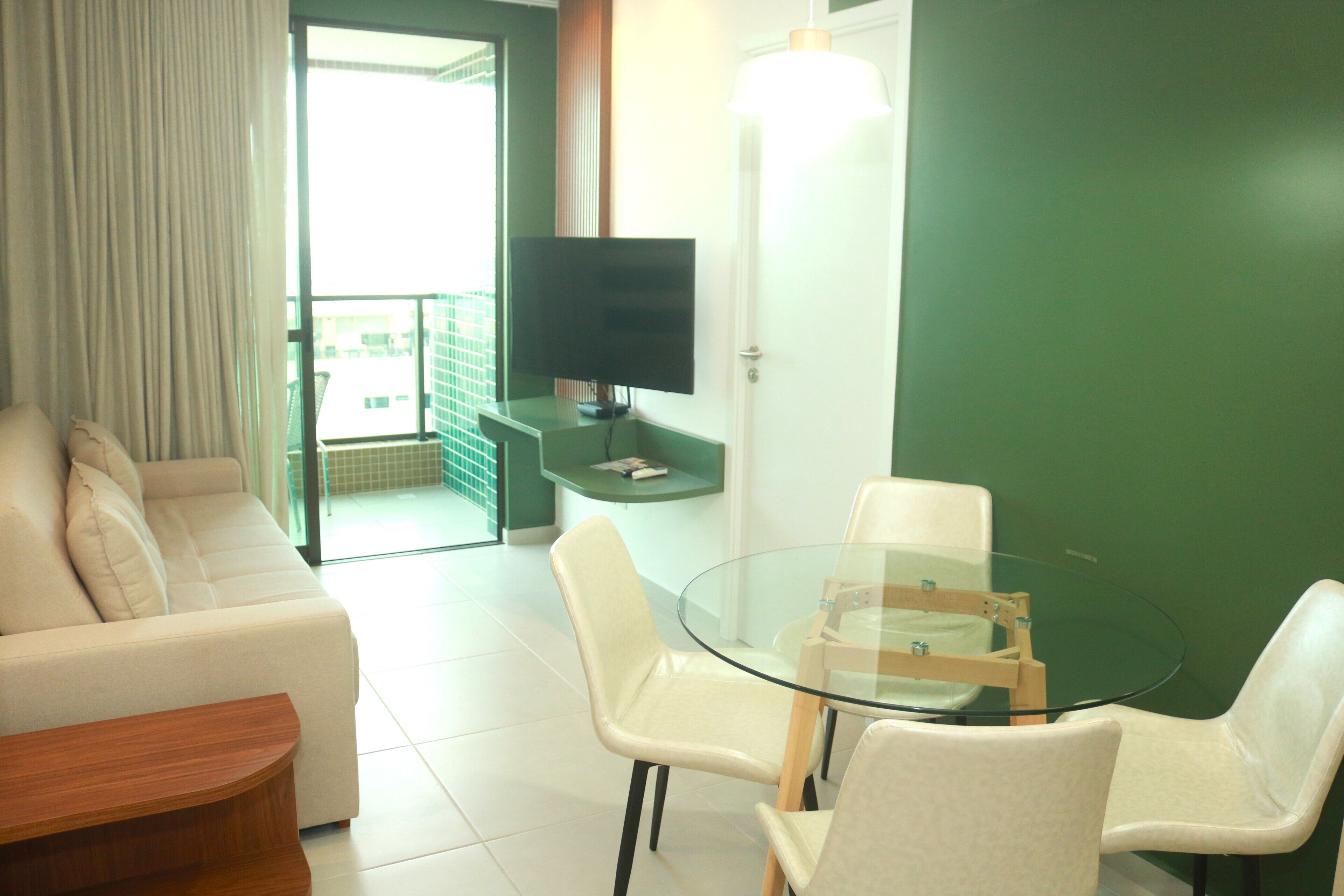 Une chambre d’hôtel moderne, dotée d’un canapé, d’une table en verre avec des chaises, d’un téléviseur à écran plat et d’un mur d’accent vert.