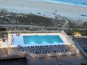 A pool area with lounge chairs and a pool, surrounded by a deck and a fence.