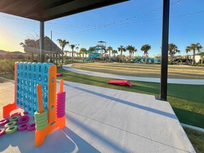 Zona de juegos al aire libre con estructuras coloridas, un sendero y un parque con palmeras y un tobogán de agua al fondo.