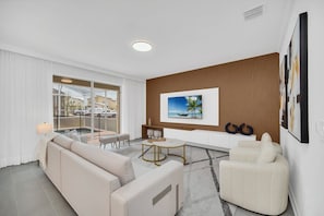 A modern living room with a sofa, armchairs, a coffee table, and a TV mounted on a wooden wall. - Superhero & Minions • Sports Game Room • South-Facing Pool & Spa • Disney (Davenport)