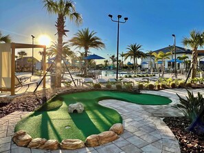 Un campo de golf con un putting green, palmeras y zonas de estar al aire libre.
