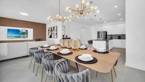 Un espace de salle à manger moderne, avec une longue table, des chaises à revêtement gris et un lustre original.