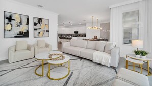 Un salon moderne avec un canapé blanc, deux fauteuils, une table basse et, au fond, un coin repas.