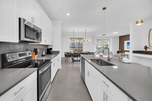 Une cuisine moderne avec des meubles blancs, des appareils en acier inoxydable et un îlot central doté d’un évier.