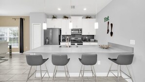 Een moderne keuken met witte kasten, roestvrijstalen apparatuur en een centraal eiland met barstoelen.