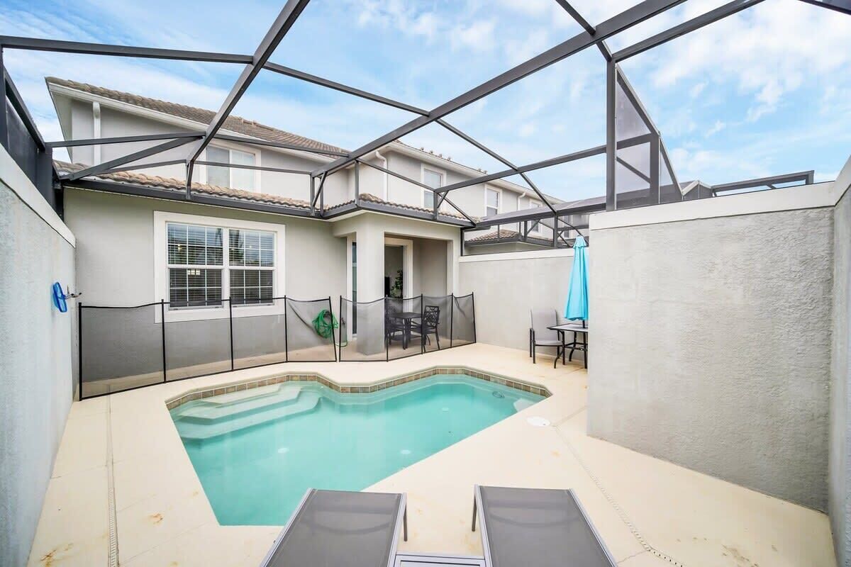 A swimming pool with a covered area, a patio with chairs, and a view of a residential building.