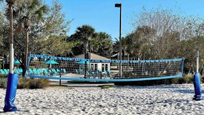 A beach volleyball net with blue padding, surrounded by sand and palm trees. - Toy Story | Mickey | Splash Pool | Near Disney 9017 (Davenport)