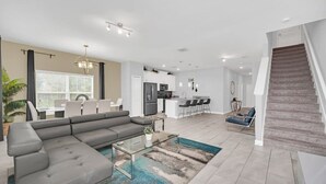 A modern living room with a sectional sofa, a glass coffee table, and a view of the kitchen and dining area. - Toy Story | Mickey | Splash Pool | Near Disney 9017 (Davenport)