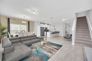 A modern living room with a sectional sofa, a glass coffee table, and a view of the kitchen and dining area.