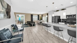 A modern kitchen with white cabinets, a black refrigerator, and a microwave. There is a dining area with a table and chairs, and a living room with a sofa and a coffee table. - Toy Story | Mickey | Splash Pool | Near Disney 9017 (Davenport)