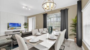 Een moderne eetruimte met een witte tafel gedekt voor zes personen, een grote decoratieve spiegel en een kroonluchter.
