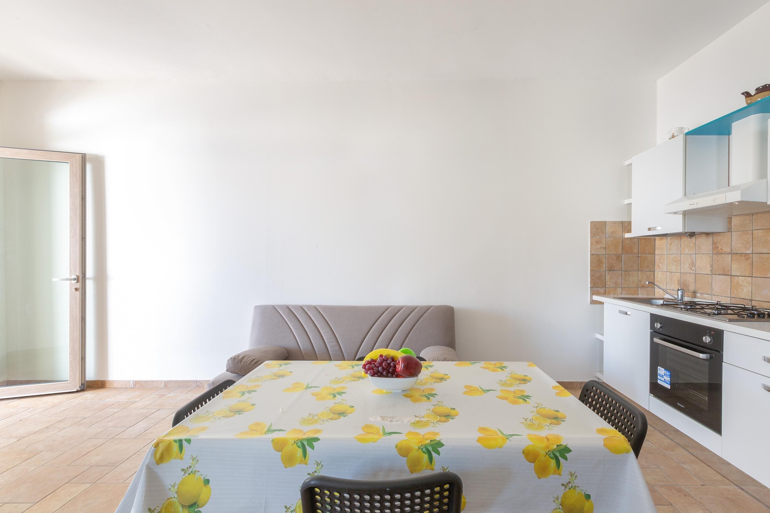 Una pequeña cocina con mesa, sillas y un frutero.