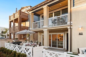 Un bâtiment à deux étages doté d’un balcon, d’un espace extérieur aménagé pour s’asseoir et d’une cuisine visible.
