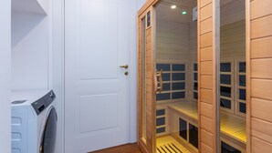 A laundry area with a washing machine, a white door, and a wooden sauna with glass panels. - Elegant Home With Sauna by Wonderful Italy (Turin)