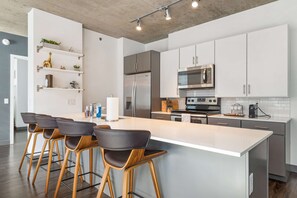 A modern kitchen with a central island, bar stools, stainless steel appliances, and white cabinetry.
