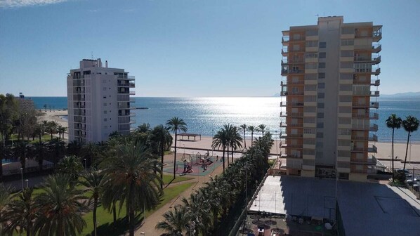 A beachfront hotel with multiple floors, a pool area, and palm trees.