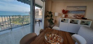 Un balcó amb vista al mar i a edificis, taula de dinar amb cadires, una planta en test i un moble amb objectes decoratius.