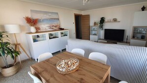 A compact living space with a dining table, two striped beds, a TV, and a cabinet with glass doors.
