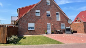 Une maison à deux étages, construite en briques, avec un toit rouge, une antenne parabolique et un petit patio aménagé avec du mobilier d’extérieur.