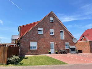 Een tweelaags bakstenen huis met een rood dak, een schotelantenne en een klein terras met tuinmeubilair.