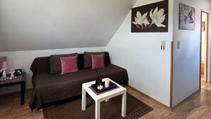Un salon chaleureux avec un canapé marron, une table basse blanche et un tapis. Deux œuvres d’art sont accrochées au mur, et un luminaire est fixé au plafond.
