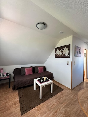 Een gezellige woonkamer met een bruine bank, een witte salontafel en een vloerkleed. Er hangen twee kunstwerken aan de muur en er is een plafondlamp.