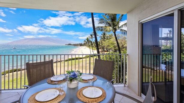 Un balcon avec une table dressée pour deux personnes, donnant sur une plage et l’océan.