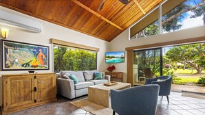 Un vaste salon doté d’un plafond en bois, d’un canapé gris, d’une table basse et d’une grande fenêtre offrant une vue sur la verdure.