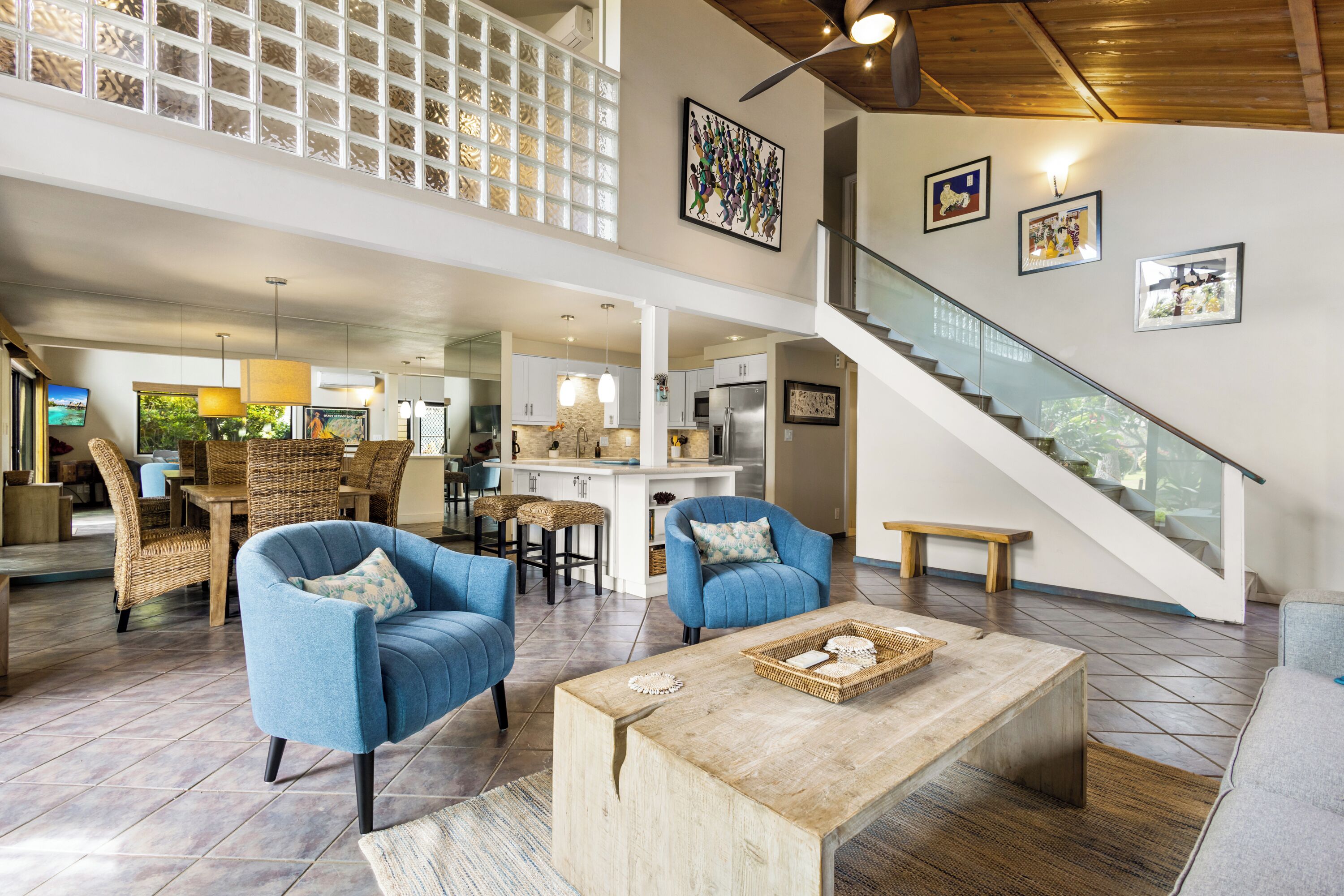 A spacious living area with a high ceiling, a staircase, and a kitchen in the background.