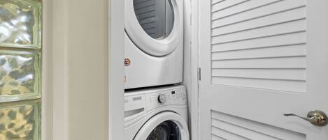 Un lavadero con dos lavadoras superpuestas y una puerta con persianas horizontales.