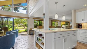 Une cuisine moderne avec des meubles blancs, un grand îlot central et des luminaires suspendus.