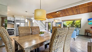 Une cuisine moderne dotée d’appareils électroménagers en acier inoxydable, une table à manger en bois avec des chaises en osier, et une grande fenêtre offrant une vue sur la verdure.