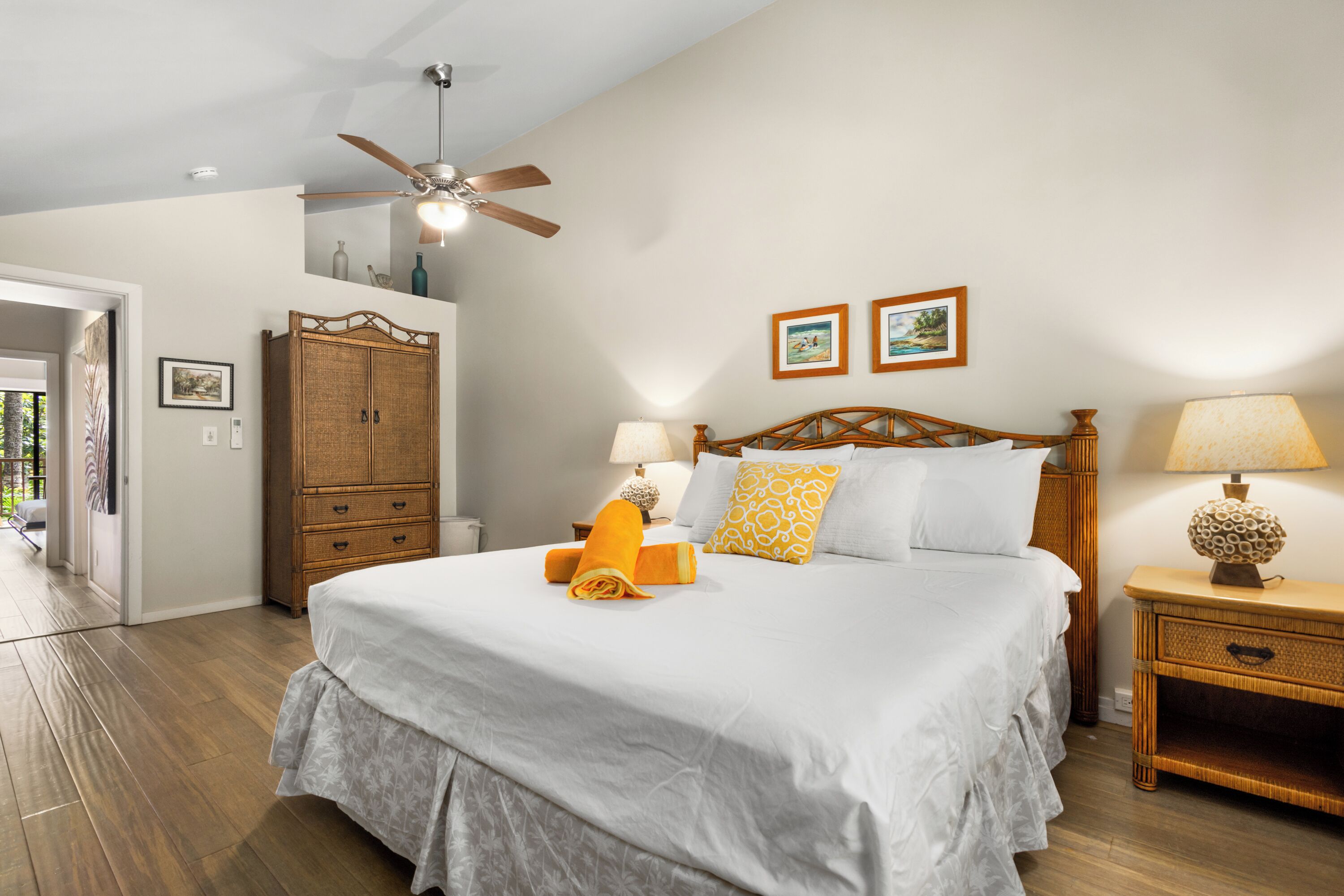 A bedroom with a large bed, wooden headboard, two bedside lamps, a ceiling fan, and a wooden wardrobe.