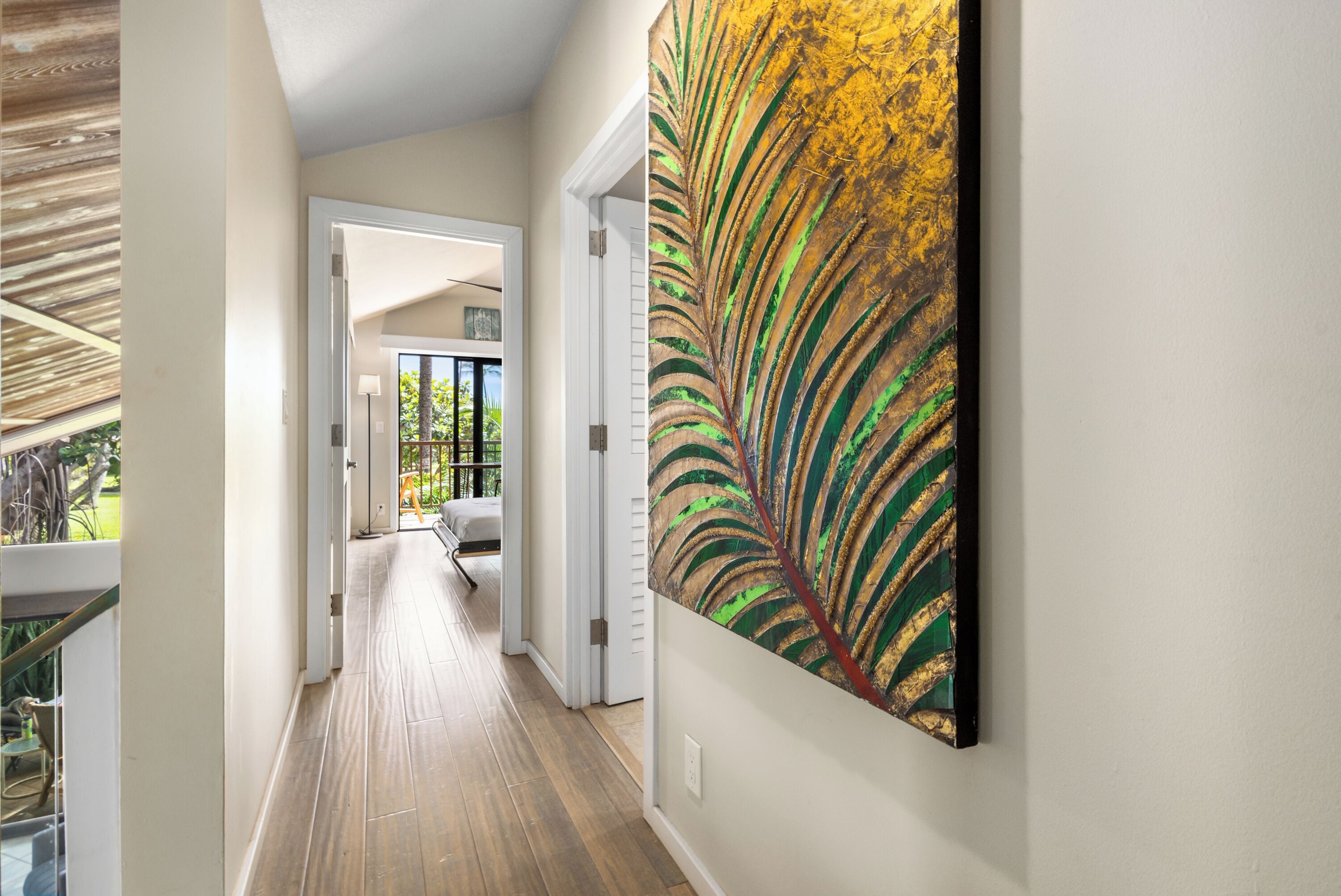 A hallway with wooden flooring, a large abstract painting on the wall, and a view of a balcony with a railing.