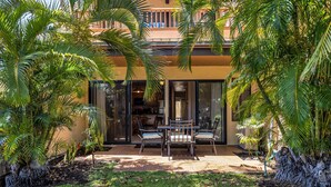 Un patio con una mesa y sillas, rodeado de palmeras y un edificio con grandes puertas de vidrio.