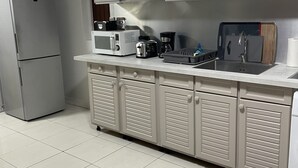 A modern kitchen with a refrigerator, microwave, toaster, coffee maker, and a sink with a cutting board.